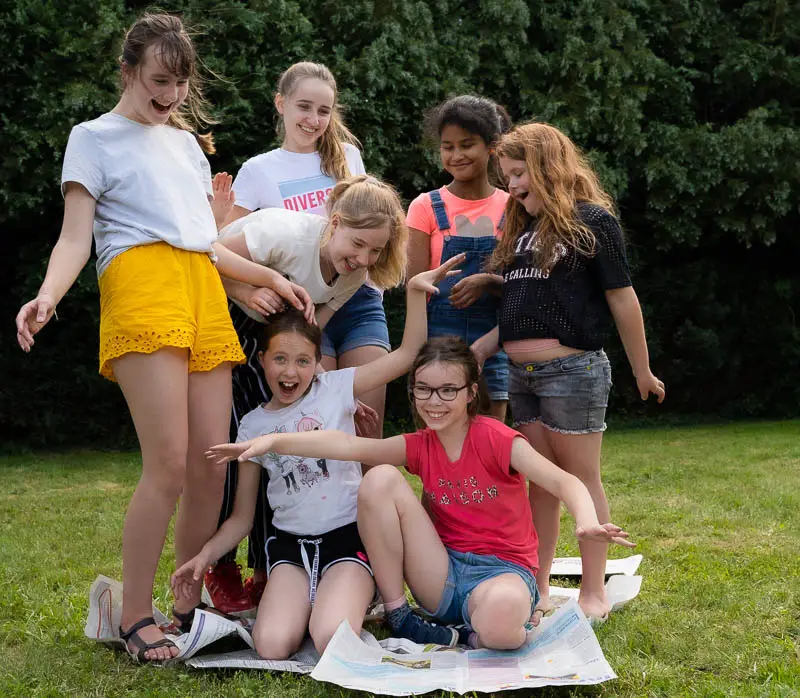 Een groep kinderen speelt buiten in het gras een scène met kranten